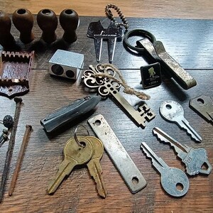 May include: A collection of miscellaneous metal and wooden items including four small wooden knobs, a silver-toned golf divot tool, a metal key ring, a small wooden tray, a silver-toned sharpener, a decorative skeleton key, a black pin, a pocket knife, several metal keys, a flat metal strip, and two long rusty nails.