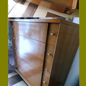 Peut inclure: Commode en bois de style moderne du milieu du si&egrave;cle dernier, avec cinq tiroirs et une armoire lat&eacute;rale avec de plus petits tiroirs. Le meuble est en bois brun clair avec des boutons argent&eacute;s. Le tiroir sup&eacute;rieur est ouvert.