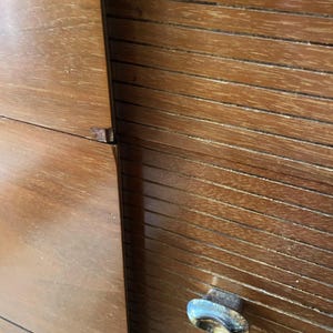 Peut inclure: Gros plan sur une armoire en bois avec une finition brun chaud. L'armoire pr&eacute;sente un design &agrave; lattes sur le c&ocirc;t&eacute; droit et une surface lisse et plate sur le c&ocirc;t&eacute; gauche. Une poign&eacute;e en m&eacute;tal terni est visible.
