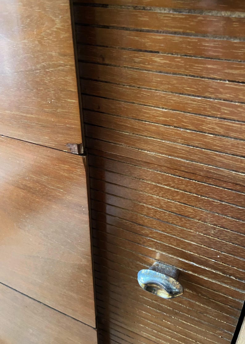 Peut inclure: Gros plan sur une armoire en bois avec une finition brun chaud. L'armoire pr&eacute;sente un design &agrave; lattes sur le c&ocirc;t&eacute; droit et une surface lisse et plate sur le c&ocirc;t&eacute; gauche. Une poign&eacute;e en m&eacute;tal terni est visible.