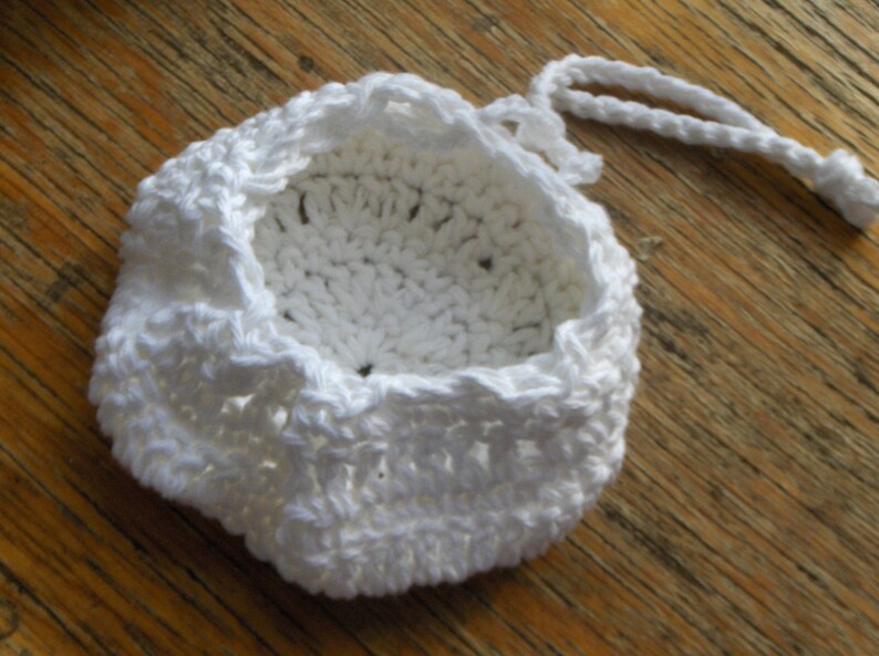 May include: White crocheted drawstring bag with a round bottom and a white cord.