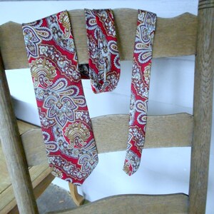 May include: Two red and gold paisley patterned neckties hanging on a wooden chair back.