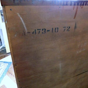 Peut inclure: Gros plan sur le c&ocirc;t&eacute; d'une armoire en bois avec le grain du bois visible. Le texte "A-473-10 72" est pochoir en noir. L'armoire semble &ecirc;tre vintage ou antique, avec une teinte marron chaude.