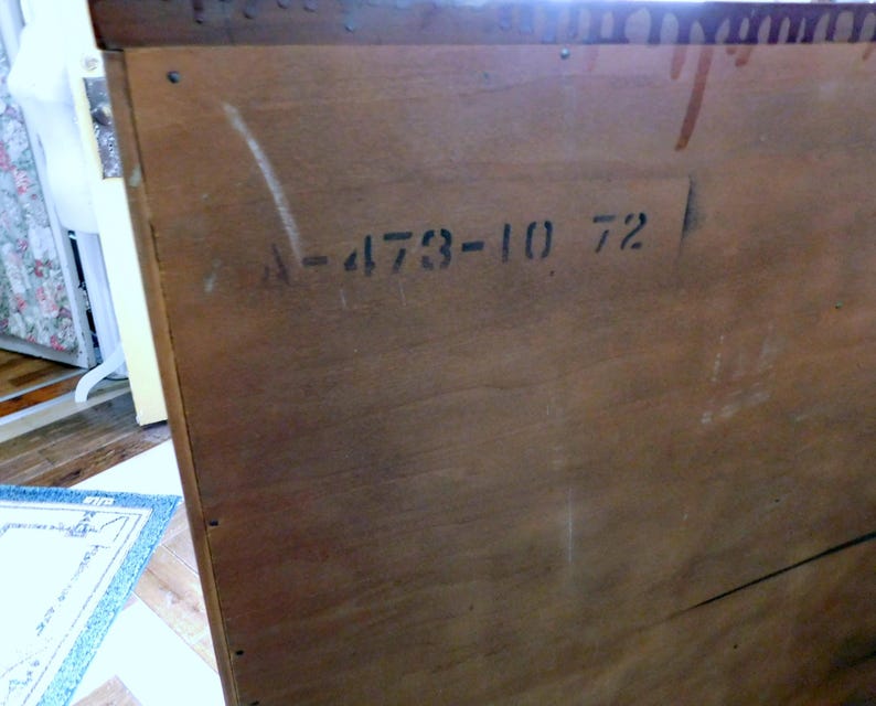 Peut inclure: Gros plan sur le c&ocirc;t&eacute; d'une armoire en bois avec le grain du bois visible. Le texte "A-473-10 72" est pochoir en noir. L'armoire semble &ecirc;tre vintage ou antique, avec une teinte marron chaude.