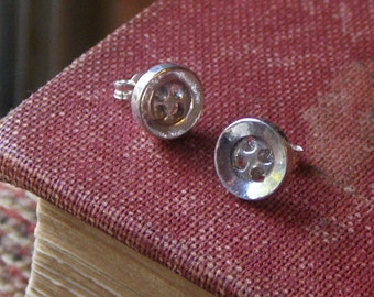 May include: A pair of silver button earrings with a circular design. The earrings have a simple, minimalist style.