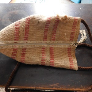 May include: A small, brown and red striped bag with a zipper closure and a brown rope strap.