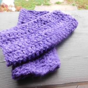 May include: A pair of purple crocheted fingerless gloves. The gloves are made with a soft, fuzzy yarn.