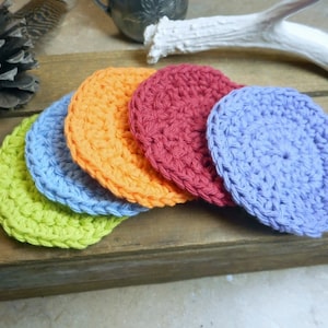 May include: Five crocheted scrubbies in different colors, including green, blue, orange, red, and purple. The scrubbies are stacked on top of each other.