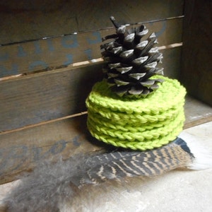 Pode incluir: Uma pilha de  coasters de croch&ecirc; verde lim&atilde;o com uma pinha no topo. Os coasters est&atilde;o sobre uma superf&iacute;cie de madeira.