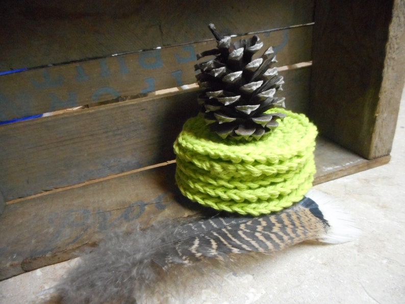 Pode incluir: Uma pilha de  coasters de croch&ecirc; verde lim&atilde;o com uma pinha no topo. Os coasters est&atilde;o sobre uma superf&iacute;cie de madeira.