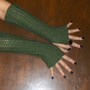 Puede incluir: Un par de guantes sin dedos de crochet verde. Los guantes son largos y llegan más allá de la muñeca. Los guantes están hechos con un patrón de punto simple.