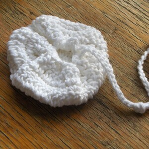 May include: White crocheted drawstring bag with a long cord. The bag is made of a soft, textured yarn and has a simple, elegant design.