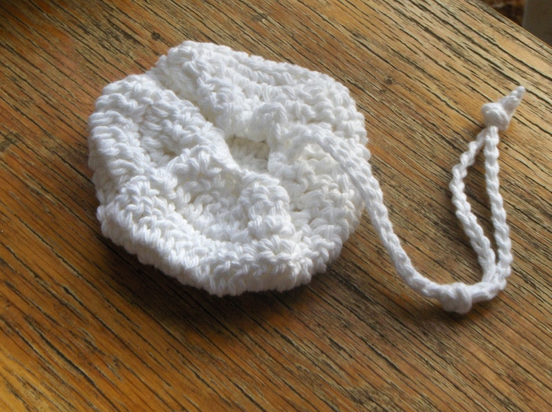 May include: White crocheted drawstring bag with a long cord. The bag is made of a soft, textured yarn and has a simple, elegant design.