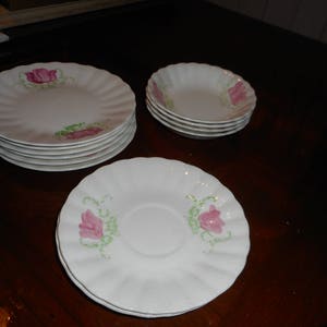 May include: A set of white ceramic plates with a pink floral design. The plates are stacked in a pyramid shape. The plates are all the same size and have a scalloped edge.