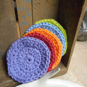 May include: A stack of six crocheted round dishcloths in rainbow colors, starting with purple, then orange, red, blue, green, and yellow.
