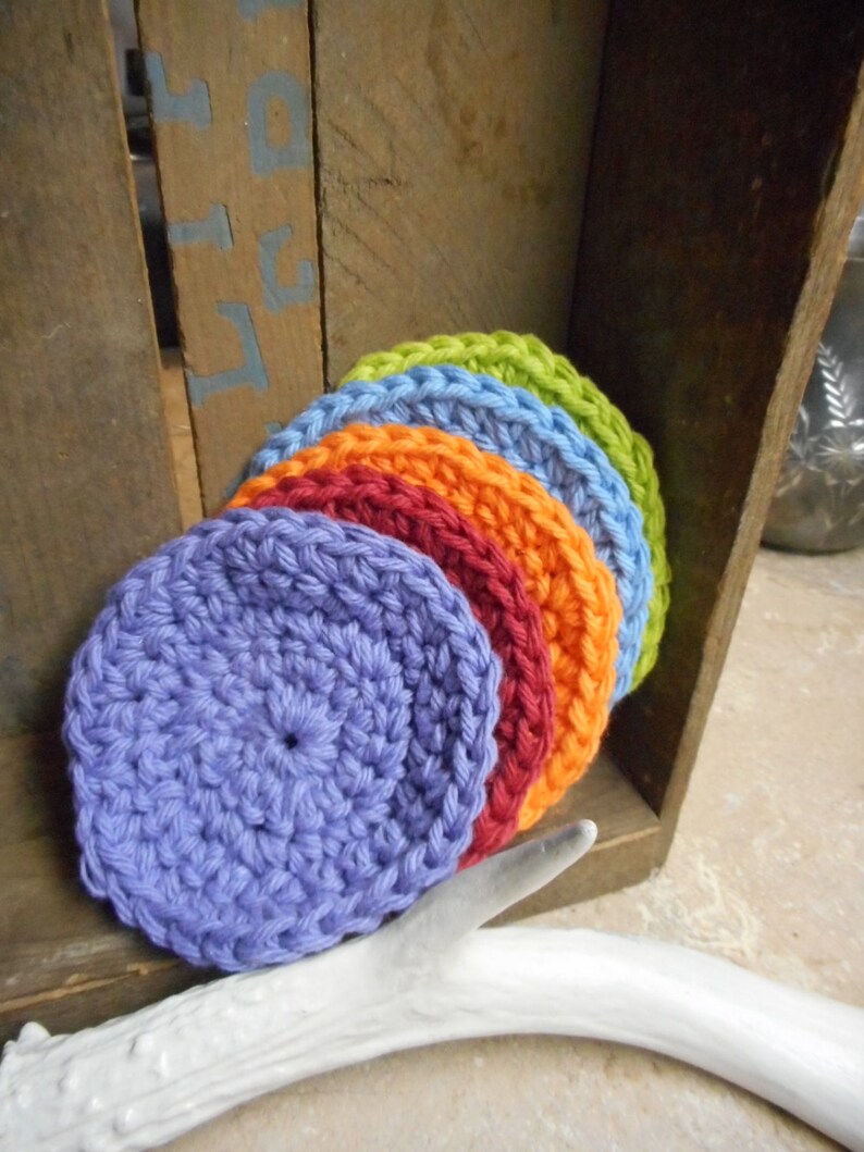 May include: A stack of six crocheted round dishcloths in rainbow colors, starting with purple, then orange, red, blue, green, and yellow.
