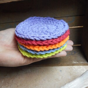 May include: A stack of six crocheted coasters in a rainbow of colors, including purple, red, orange, light blue, green, and yellow.