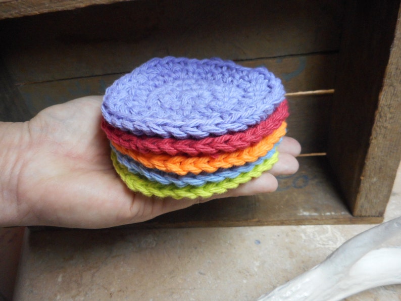 May include: A stack of six crocheted coasters in a rainbow of colors, including purple, red, orange, light blue, green, and yellow.