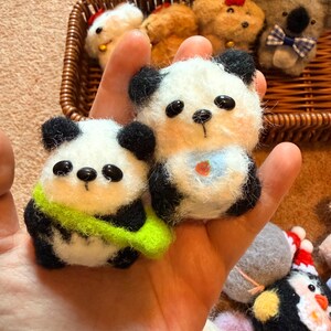 May include: Handmade felt panda bear and other animal ornaments. The panda bears are white with black accents and have small black eyes. One panda has a green scarf, and the other has a blue bib. Other animals include a koala, dogs, and a penguin.