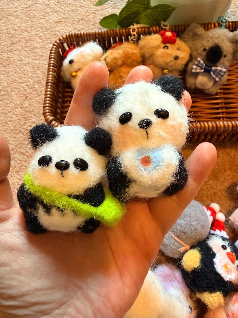 May include: Handmade felt panda bear and other animal ornaments. The panda bears are white with black accents and have small black eyes. One panda has a green scarf, and the other has a blue bib. Other animals include a koala, dogs, and a penguin.