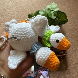 Puede incluir: Llaveros de ganso de ganchillo en blanco, naranja, verde y azul. Los llaveros presentan costuras detalladas, con algunos gansos que llevan bufandas. Tambi&eacute;n se ven otras figuras de ganchillo coloridas.