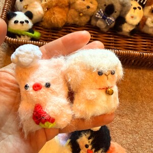 May include: A collection of handmade felt animal keychains, including a panda, koala, and various other creatures. The keychains are in a woven basket. The keychains are in various colors, including white, pink, brown, and black. The pig keychain has a watermelon design.