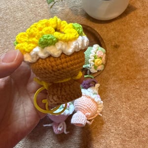 Pu&ograve; includere: Portachiavi a forma di cupcake all'uncinetto con glassa gialla, verde e bianca. Il cupcake ha una base marrone e un portachiavi giallo. Sono visibili anche altri cupcake all'uncinetto rosa e verdi.