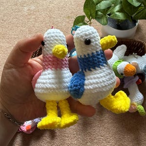 Puede incluir: Dos llaveros de pato hechos a mano con ganchillo. Un pato tiene el cuello rosa y el otro una franja azul. Ambos tienen cuerpos blancos, picos y patas amarillas y ojos negros. Los llaveros est&aacute;n hechos de hilo suave.