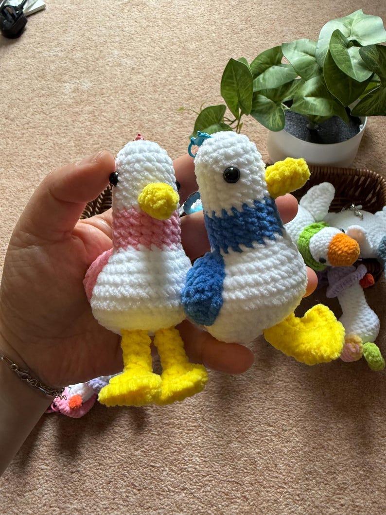 Puede incluir: Dos llaveros de pato hechos a mano con ganchillo. Un pato tiene el cuello rosa y el otro una franja azul. Ambos tienen cuerpos blancos, picos y patas amarillas y ojos negros. Los llaveros est&aacute;n hechos de hilo suave.