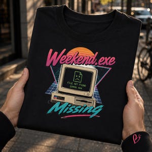 May include: A black t-shirt featuring a retro computer graphic with the text Weekend.exe and Missing. The screen displays a sad file icon with the text FILE NOT FOUND ERROR 404. The design includes a sunset, a grid pattern, and vibrant colours.