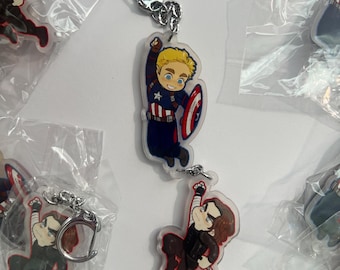 May include: A collection of clear acrylic keychains featuring cartoon-style illustrations of characters in dynamic poses. One keychain depicts a blonde character in a blue and red suit with a shield, while another shows a dark-haired character in black.
