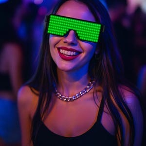 Puede incluir: Una persona sonriente con gafas LED con montura negra que muestran luces verdes. La persona también lleva un collar de cadena dorada y una camiseta sin mangas negra. El fondo está borroso con iluminación azul y púrpura, lo que sugiere una fiesta o un club.