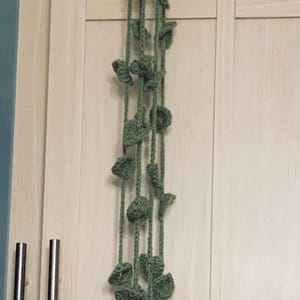 Peut inclure: Une guirlande en crochet verte avec des formes de feuilles suspendues à un mur.
