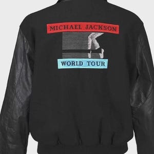 May include: Black jacket with leather sleeves. The back features a red rectangle with "MICHAEL JACKSON" in white text above a graphic and a blue rectangle with "WORLD TOUR" in white text.