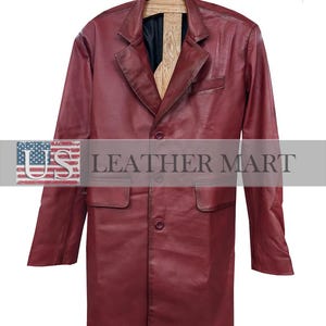 Könnte beinhalten: Ein burgunderfarbener Ledermantel mit klassischem Design. Der Mantel hat ein fallendes Revers, zwei Vordertaschen und einen Dreiknopfverschluss. Der Mantel hängt an einem Holzkleiderbügel. Der Text "US LEATHER MART" steht unten.