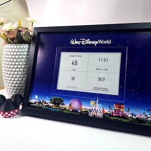 May include: A black framed digital display featuring the Walt Disney World logo at the top. The screen shows a grid with Jungle Cruise wait time of 45 minutes, the time 11:21, date WED 1 JUL, 30 days until Disney, and 75°F weather information.