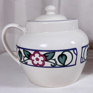 May include: White ceramic sugar bowl with a lid and handle. The bowl features a decorative band with a floral and leaf design in pink, green, and blue. The lid has a small knob.