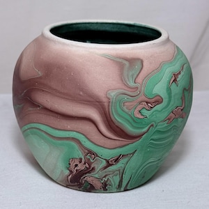 Può includere: Un vaso rotondo in ceramica con un design marmorizzato. Il vaso presenta una miscela di tonalità rosa, marrone e verde. L'interno è verde scuro e il bordo è bianco. Il vaso ha una forma liscia e arrotondata.