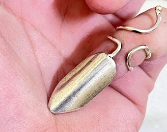 May include: A silver-toned metal ring and a pendant with a teardrop shape. The pendant has a loop at the top. The ring has a curved design. The items are displayed on a hand.