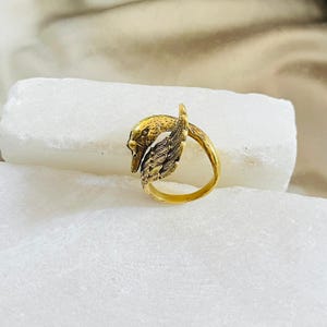 Op de afbeelding: Een goudkleurige ring met een zwanenontwerp. De kop van de zwaan en een gedetailleerde vleugel zijn zichtbaar, met de band van de ring die de basis vormt. De ring staat tegen een witte achtergrond.