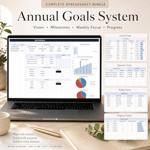 May include: A laptop displays an "Annual Goals System" spreadsheet with sections for vision, milestones, and weekly focus. Additional charts and tables show annual, quarterly, and weekly progress. A gold pen and a notebook are on the table.