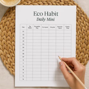 May include: A white paper titled "Eco Habit Daily Mini" with a grid for tracking daily habits. A hand holds a pencil, ready to fill in the chart. The image includes a cup of coffee and a woven placemat. The text "Engussuststainable routines" is at the bottom.