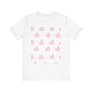 Peut inclure: Un t-shirt blanc à manches courtes orné d'un motif répétitif de cœurs rose clair imprimés au centre. Le vêtement présente une encolure ronde et une coupe standard, avec le motif de cœurs disposé en grille sur la zone de la poitrine.