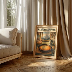 Könnte beinhalten: Ein gerahmter Druck mit dem Text "Kartoffelpuffer" in einer Raumszene. Das Kunstwerk zeigt eine Pfanne mit Kartoffelpuffern, ein Fenster mit Bergblick und einen Bierkrug. Der Rahmen ist aus hellem Holz.