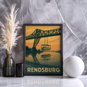 Könnte beinhalten: Gerahmter Kunstdruck mit einer Illustration im Vintage-Stil der Rendsburg Hochbrücke über einem Fluss, mit einer Gondel. Das Kunstwerk hat eine warme Farbpalette aus Orange, Grün und Blau. Das Wort "RENDSBURG" ist unten aufgedruckt.