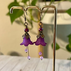 May include: Purple flower shaped earrings with a red crystal bead and dangling pink crystals.