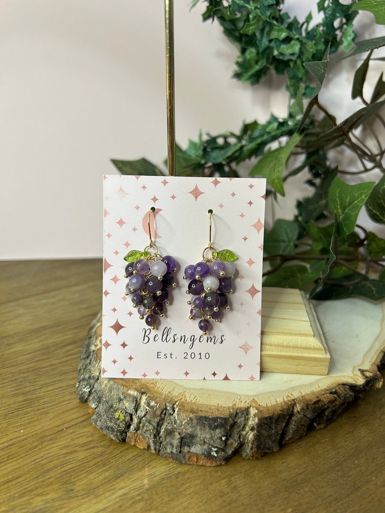 May include: Amethyst grape earrings with gold accents and green leaves. The earrings are on a white card with the text "Bellsngems Est. 2010".