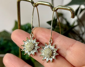 May include: A pair of gold dangle earrings with a sunflower design. Each sunflower is made of clear rhinestones and has a gold center.