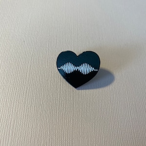 Puede incluir: Pin de esmalte negro en forma de coraz&oacute;n con un gr&aacute;fico de onda sonora blanca. La onda sonora es una representaci&oacute;n estilizada del logotipo de la banda The 1975.