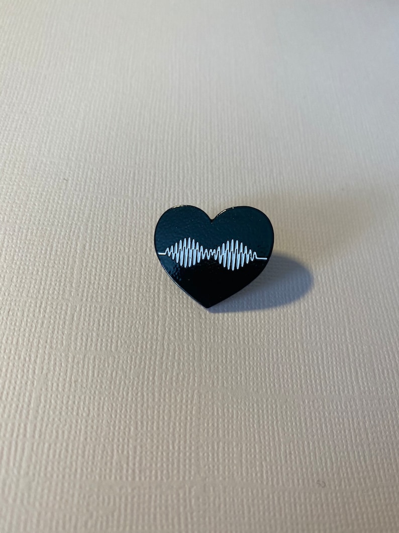 Puede incluir: Pin de esmalte negro en forma de coraz&oacute;n con un gr&aacute;fico de onda sonora blanca. La onda sonora es una representaci&oacute;n estilizada del logotipo de la banda The 1975.